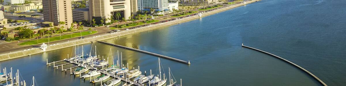 Panorama aerial view Bayfront area of Corpus Christi with skylines and marina piers row of boat, sailboat and yacht at sunrise. City harbor bridge far right in distance. A Texas city on Gulf of Mexico