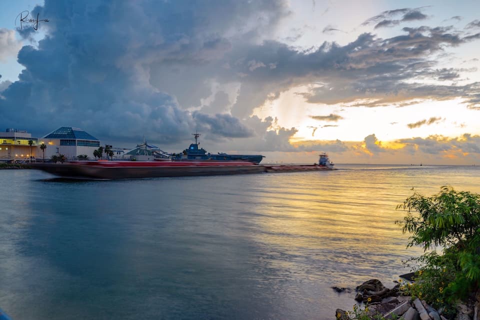 A large ship docked at a port with a modern building and a cloudy sky.