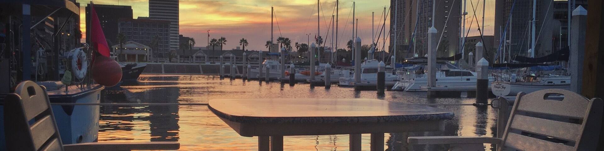 On a work-road trip to McAllen, Texas I had the opportunity to swing by Corpus Christi and grab dinner. No parading, no shopping planned, just a quick bite before seeing more freeway. I wasn't expecting to see very much.
Boy, was I surprised. We stopped for dinner just 4 miles off our route at Harrison's in Corpus Christi. We sat in the "floating" seating, a roped off dock with tables and chairs, and enjoyed some of the town's talented musicians singing homegrown versions of Sublime songs. The sun set with beautiful yellow and orange colored clouds reflected in the water and I was amazed no others were photographing this beautiful scene. Maybe indifferent, or maybe used to the beauty that is this town, and us the tourists making ourselves clearly known.
Thank you Corpus Christi for your beauty and your meal. I'm sorry our stay was rushed, we will definitely be back!