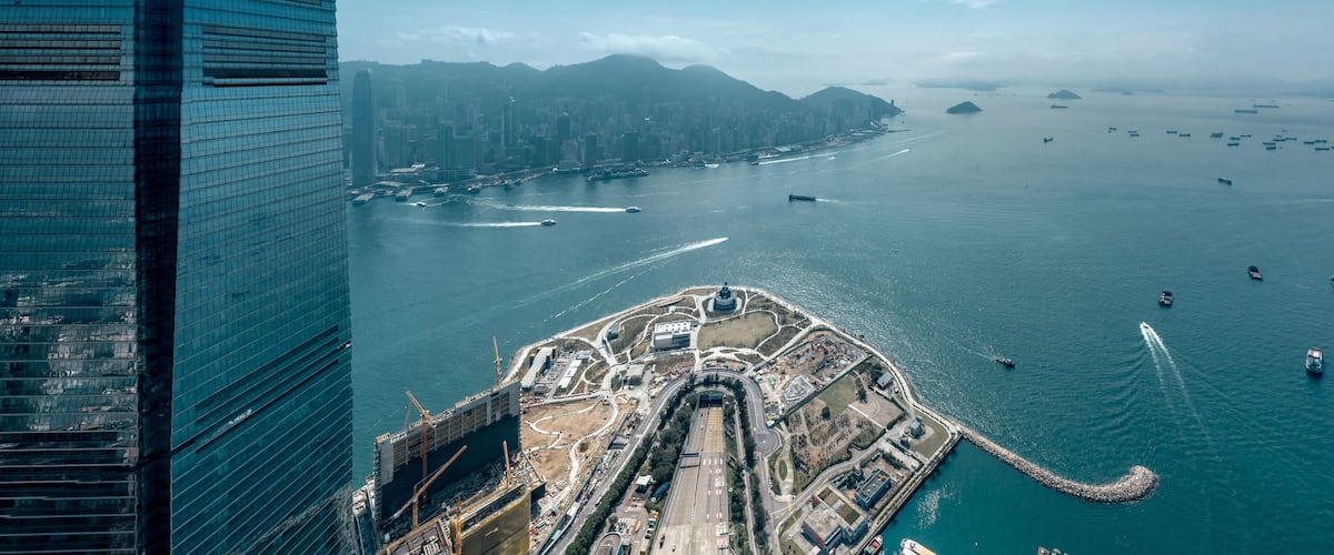 An aerial view of a coastal city with a prominent waterfront, a large port, and a mountain range in the background.