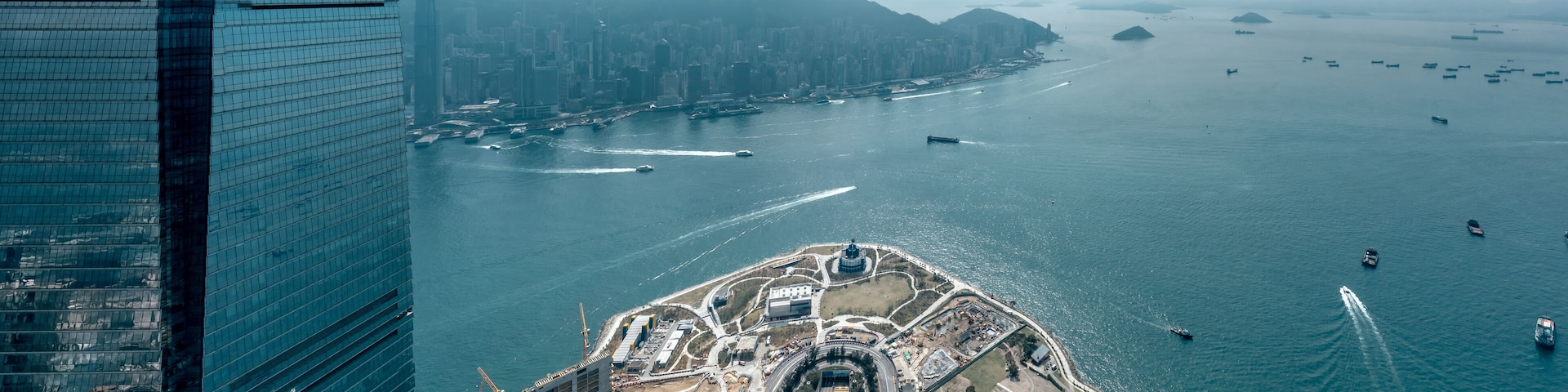 An aerial view of a coastal city with a prominent waterfront, a large port, and a mountain range in the background.