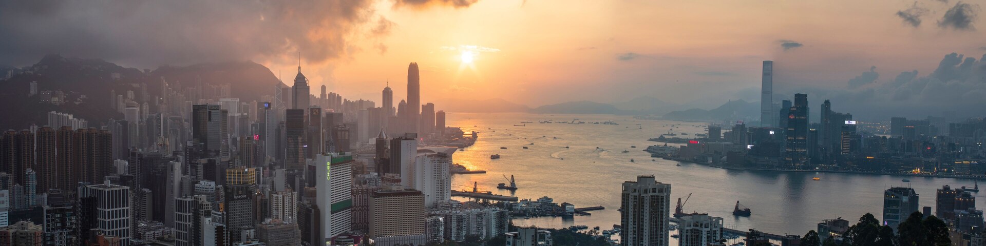 Paisagem urbana com edifícios altos, um corpo d'água e um pôr do sol.