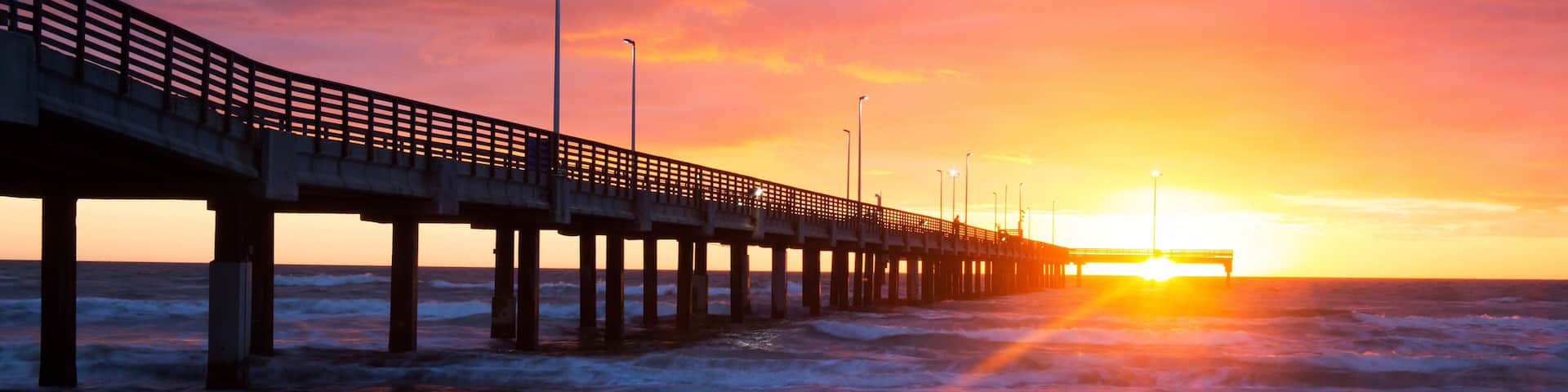 Un muelle se adentra en el océano al atardecer, con olas rompiendo contra él.