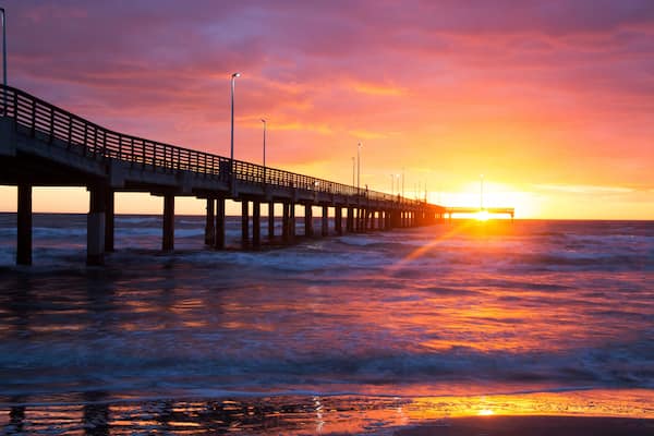 A pier extending into the ocean at sunset with waves crashing against it.