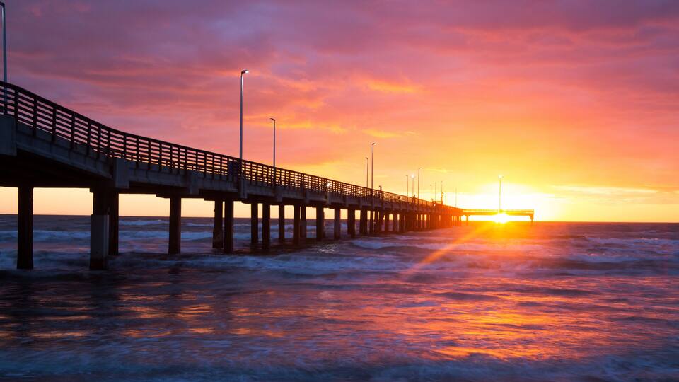 A pier extending into the ocean at sunset with waves crashing against it.
