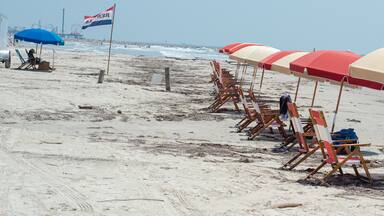Panorama view tourist couple after row of colorful rental umbrella capture managed beach areas community-friendly coastal recreation along quiet sandy shoreline, rocky pier in Galveston, Texas