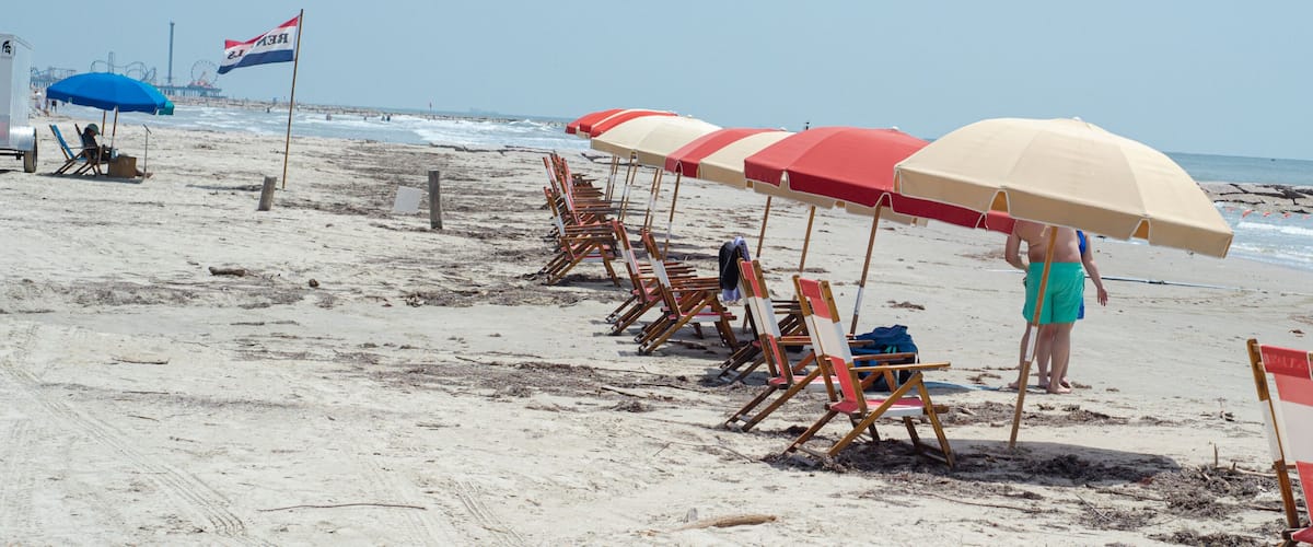 A beach with rows of beach chairs and umbrellas, a flag, and the ocean in the background.