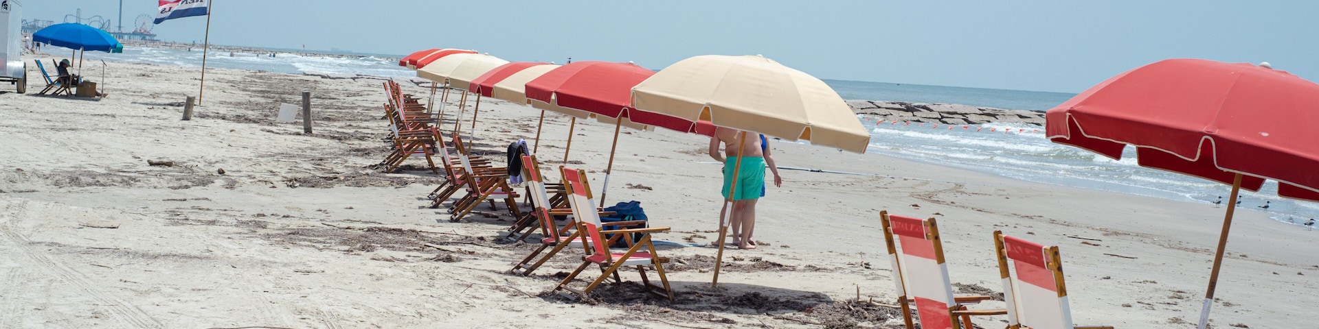 A beach with rows of beach chairs and umbrellas, a flag, and the ocean in the background.