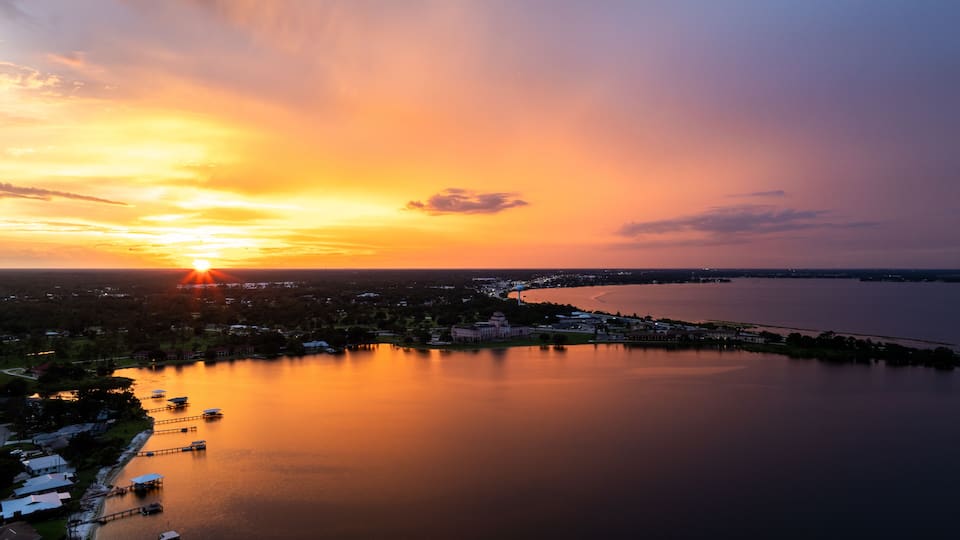 A sunset over a calm lake with a town in the foreground and a bridge extending into the water.