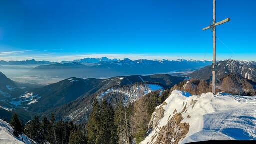 Majestic wooden cross of mountain peak Kobesnock in Gailtal Alps, Bleiberger Erzberg, Carinthia, Austria. Panoramic view of snow capped mountains of Julian Alps and Higher Tauern. Winter wonderland