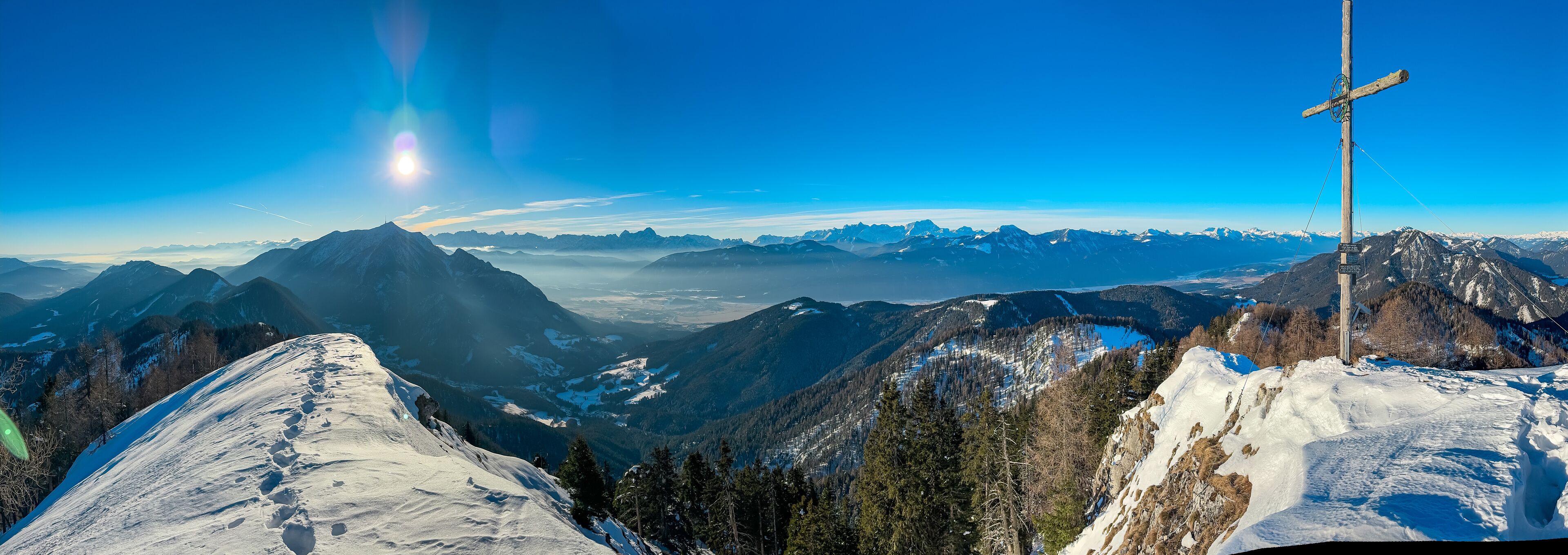 A snow-covered mountain range with a clear sky and a wooden cross structure.