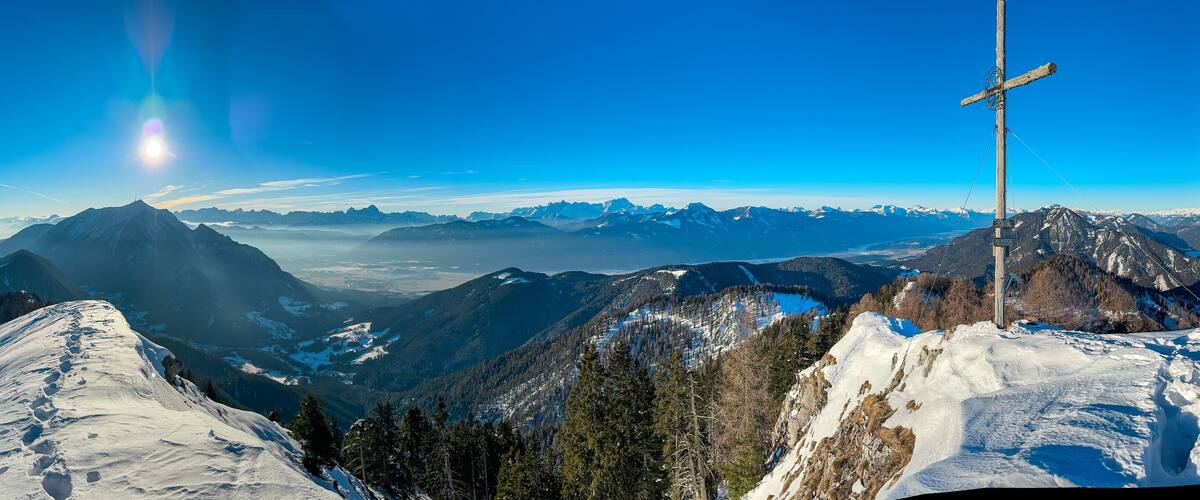 A snow-covered mountain range with a clear sky and a wooden cross structure.