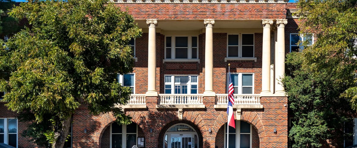 A historic brick building with columns, a flag, and a sign indicating it's a county courthouse.