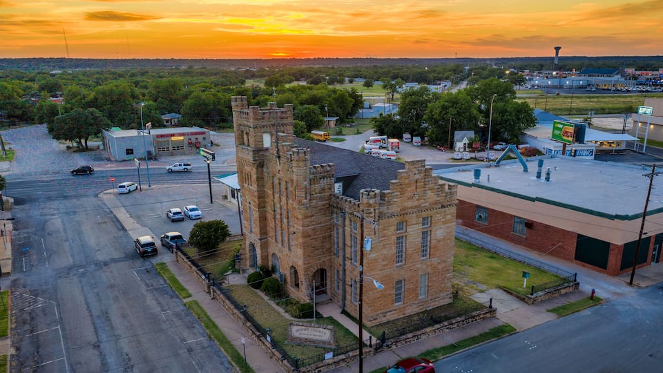 A historic building with a tower, surrounded by a parking lot and a road.