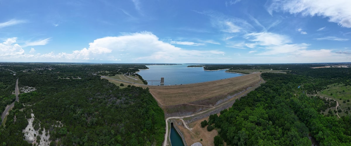 A large dam with a reservoir, surrounded by dense forests and a clear sky.