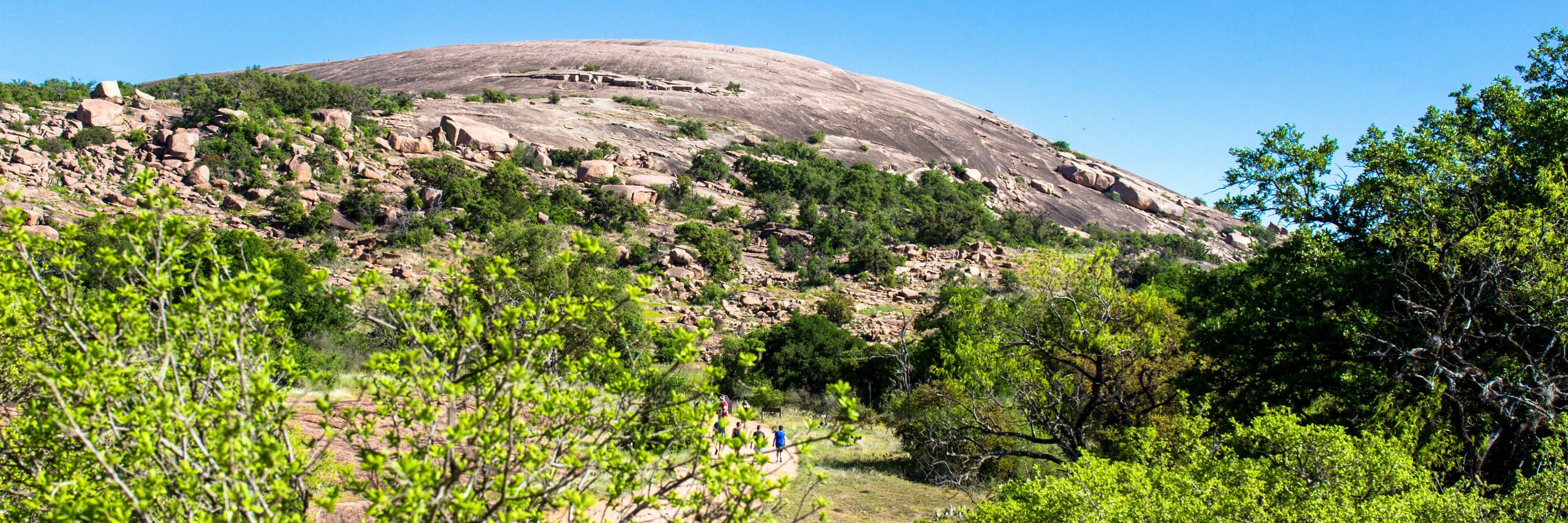 Panorama showing hikers on a trail at Enchanted Rock State Natural Area near Fredericksburg, Texas