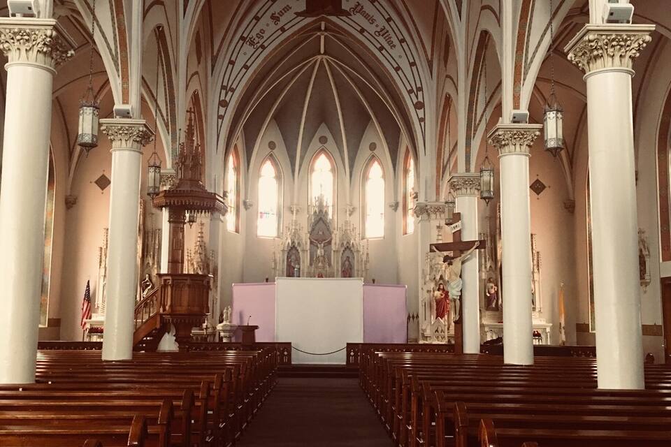 A church interior with arched ceilings, wooden pews, and a central altar.
