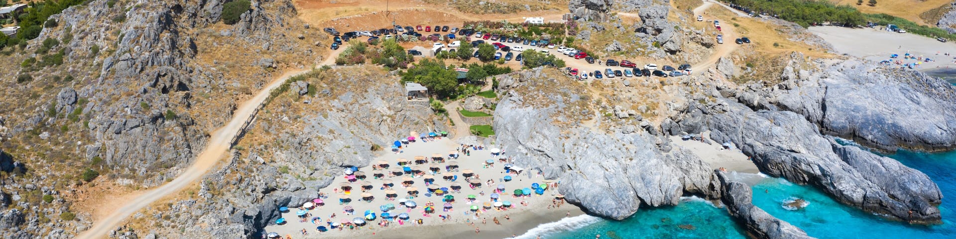 An aerial view of a coastal area with a beach, rocky cliffs, and clear blue waters.