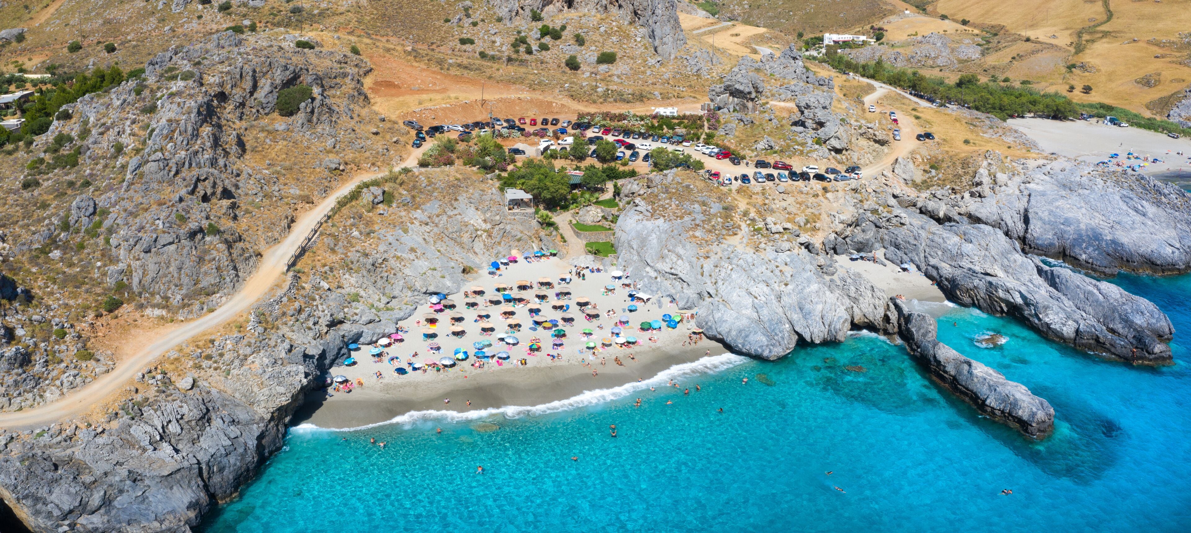 An aerial view of a coastal area with a beach, rocky cliffs, and clear blue waters.