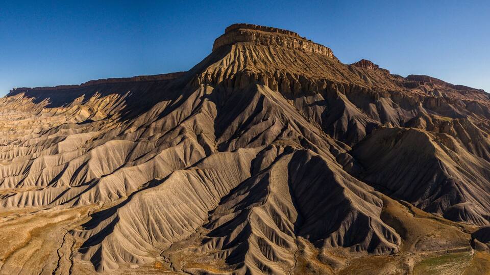 A rugged mountain range with a prominent peak, a winding road, and a flat valley.