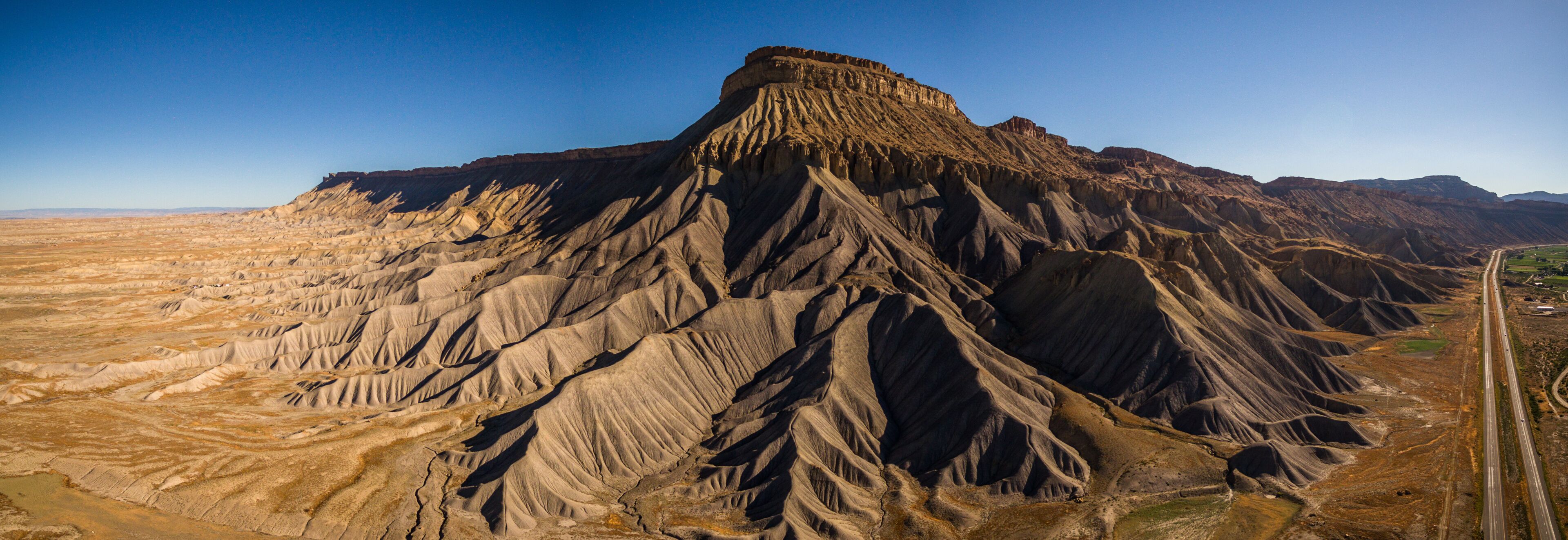 A rugged mountain range with a prominent peak, a winding road, and a flat valley.