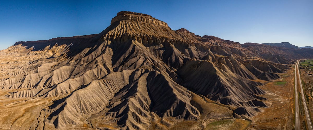 A rugged mountain range with a prominent peak, a winding road, and a flat valley.