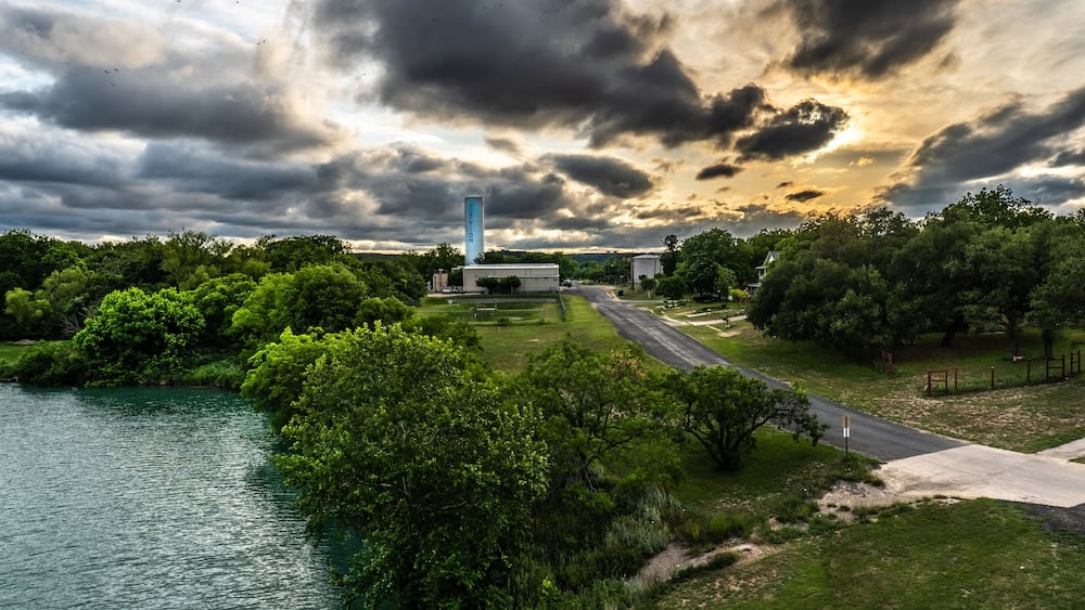 A water plant by a river and a rural road in a tree filled scenery. Junction, Texas