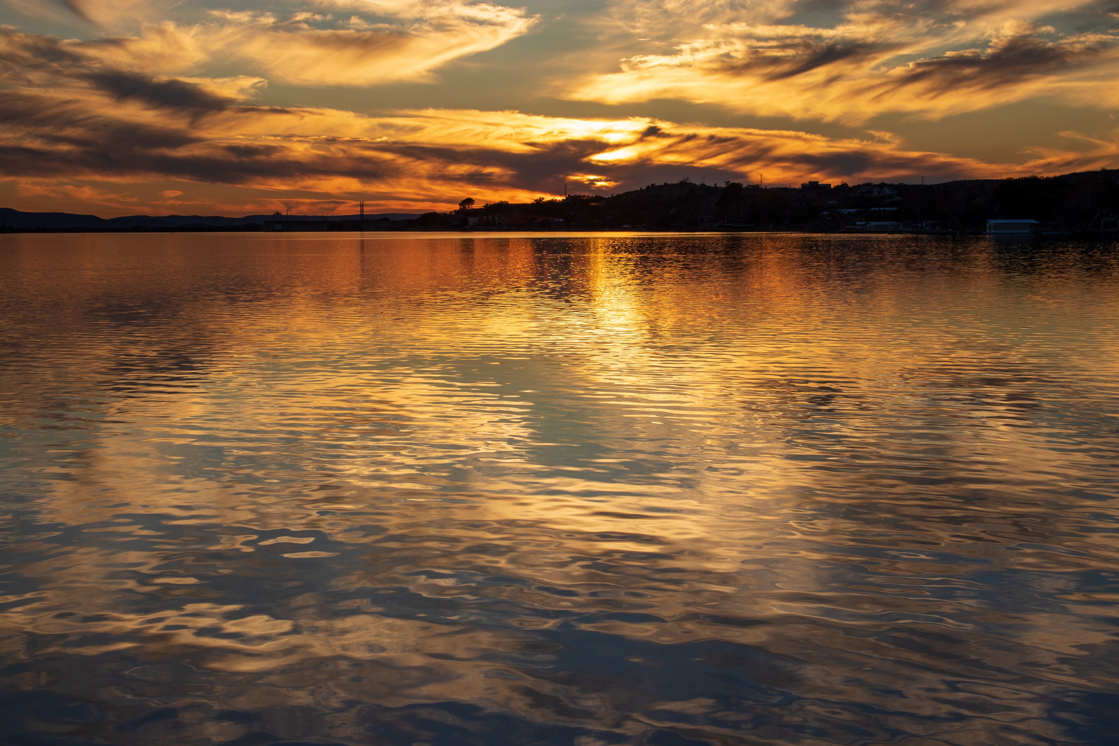A beautiful sunset over the lake with reflections of the sun and clouds on the still water serene shadowy landscape at Inks Lake State Park, Burnet TX Celebrating 100 Years.