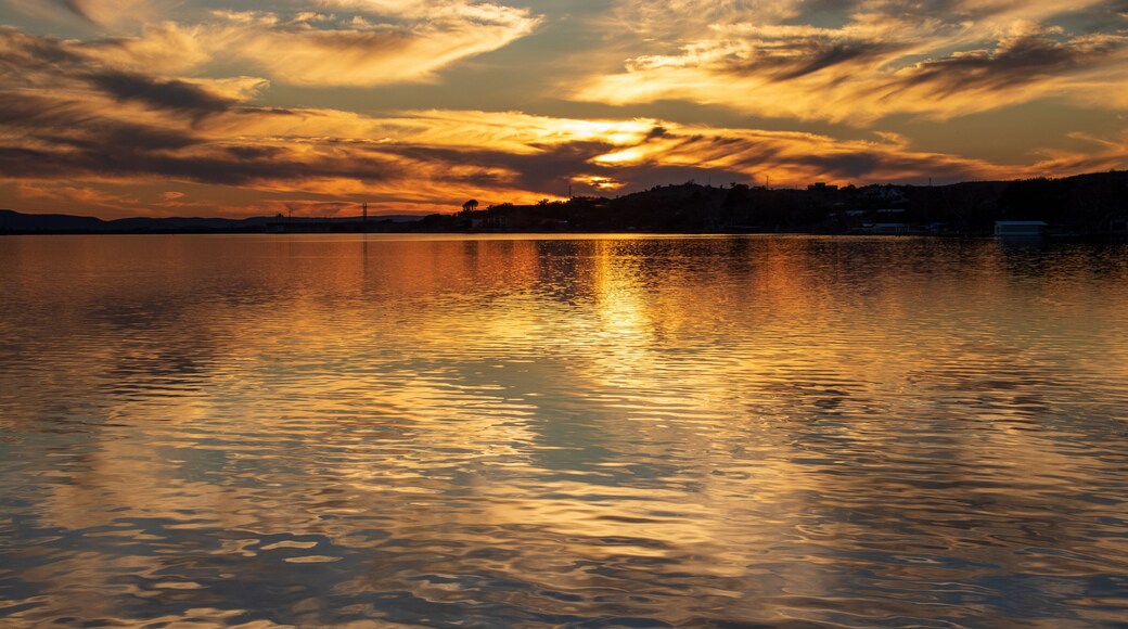 A beautiful sunset over the lake with reflections of the sun and clouds on the still water serene shadowy landscape at Inks Lake State Park, Burnet TX Celebrating 100 Years.