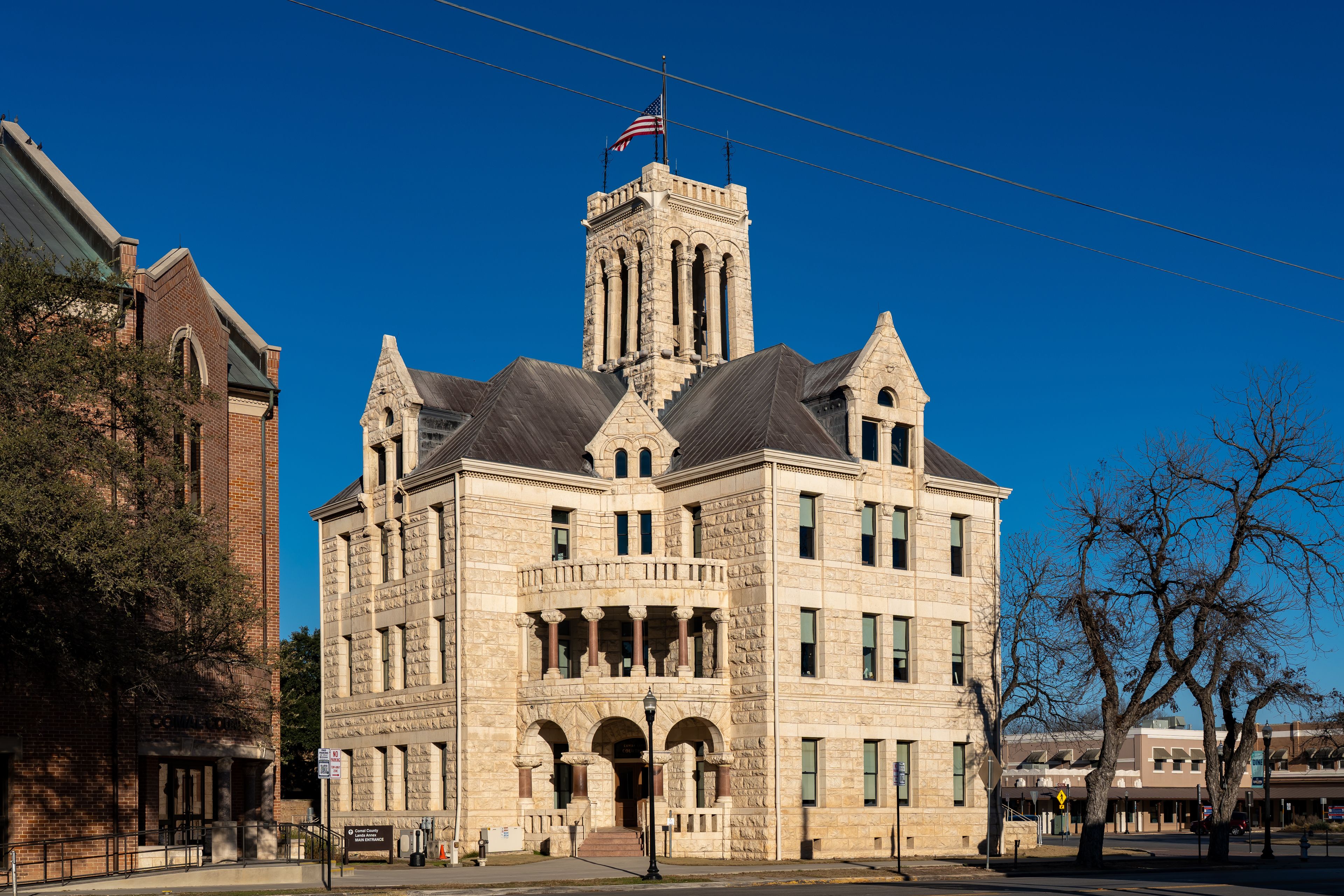 A historic courthouse with a prominent clock tower, surrounded by modern buildings and a clear blue sky.
