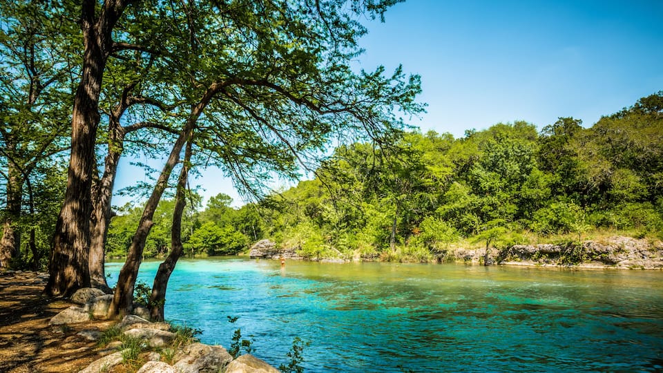 A clear turquoise river surrounded by lush green trees and rocks.