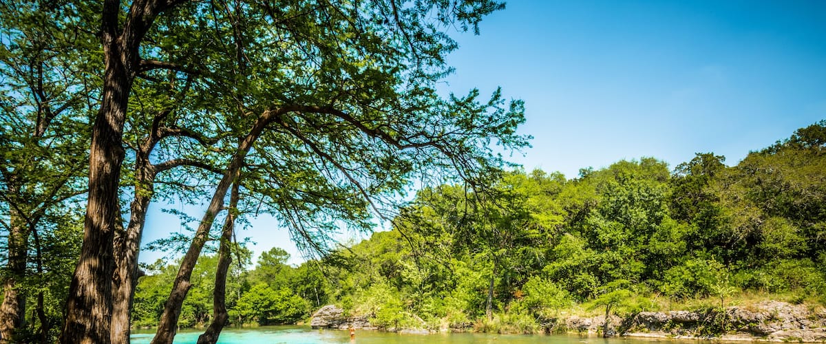 A clear turquoise river surrounded by lush green trees and rocks.