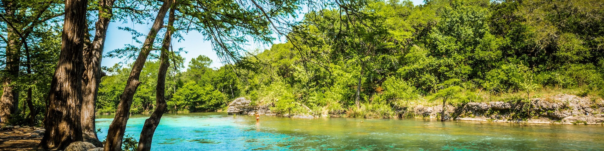 A clear turquoise river surrounded by lush green trees and rocks.