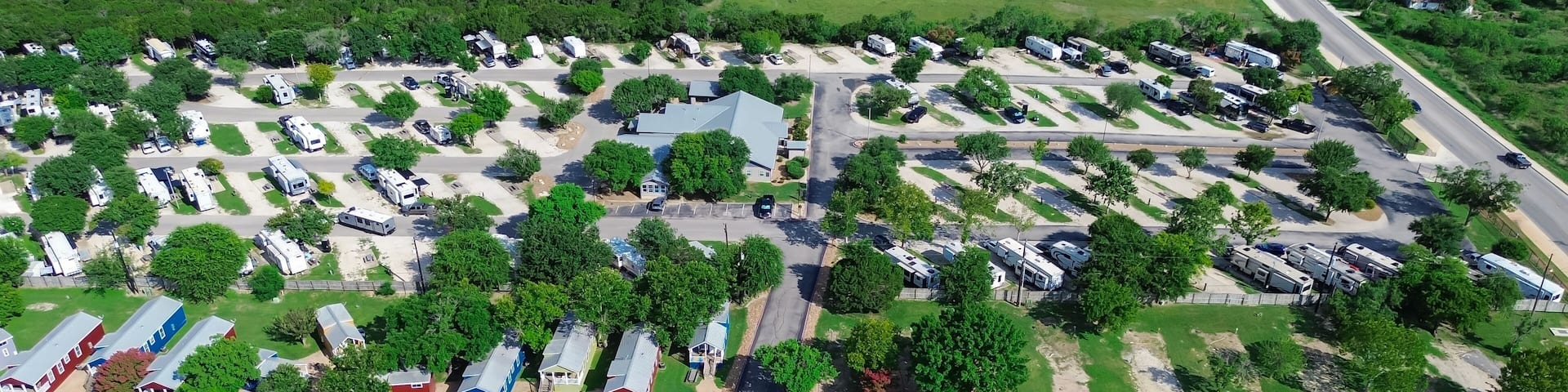 Panorama aerial view row of colorful cottage mobile home retreat vacation rentals, full hookup RV site in New Braunfels, Texas Hill Country, concrete pads electric service suburb San Antonio