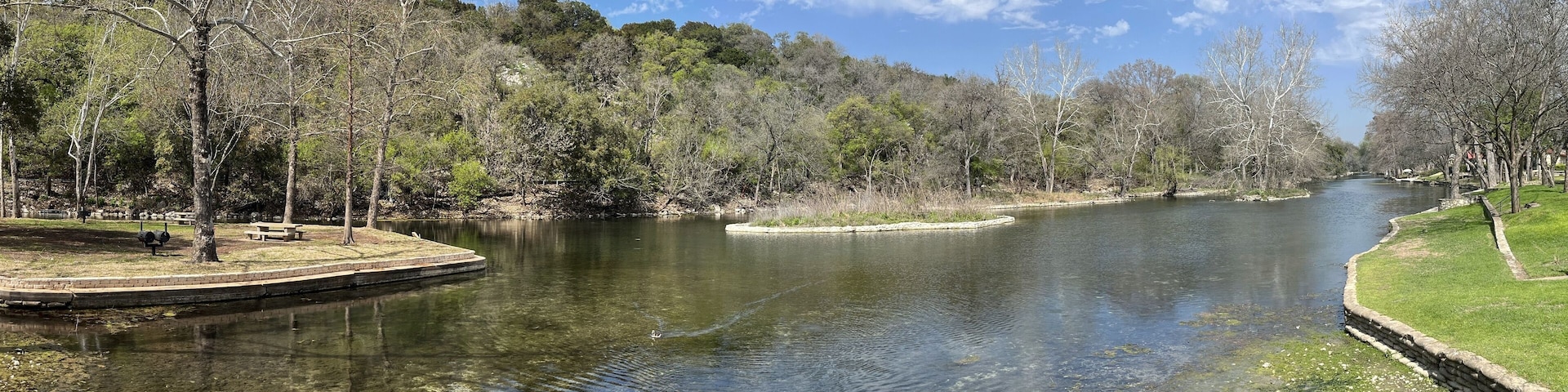 A river with clear water, surrounded by trees and grassy areas.
