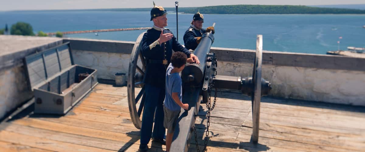A wooden deck with a cannon, two uniformed individuals, and a child.