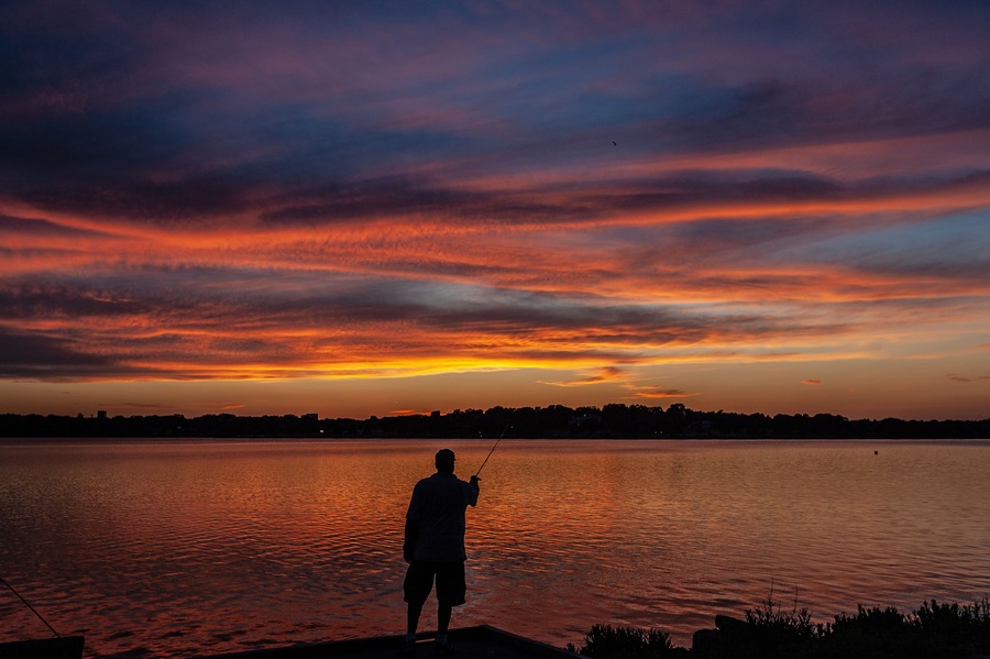 A person fishing at sunset with a vibrant sky.