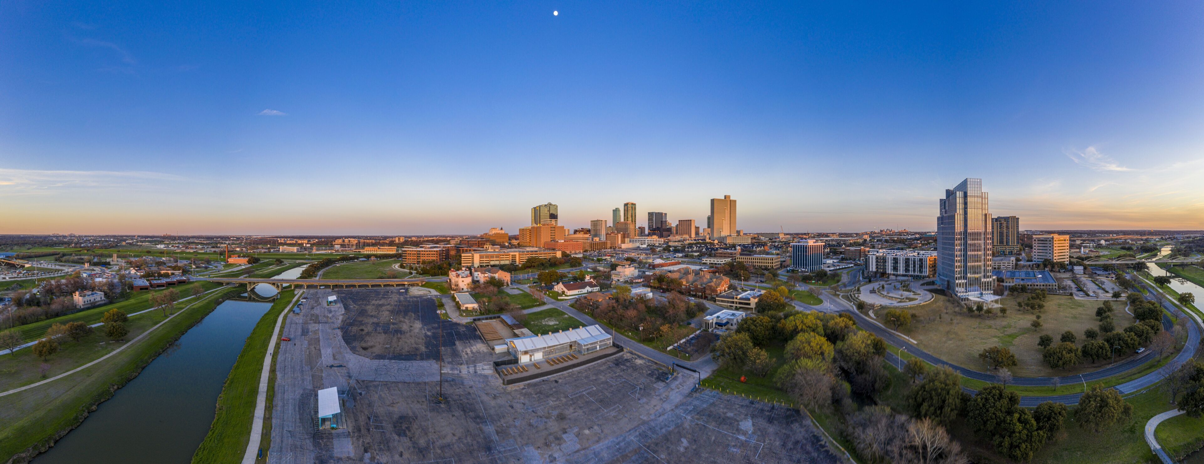 A city skyline with modern buildings, a river, and a large open construction site.