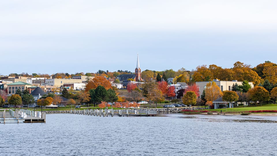 A waterfront cityscape with autumn foliage, a prominent church steeple, and a marina.