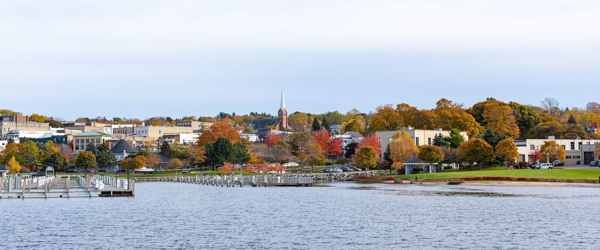 A waterfront cityscape with autumn foliage, a prominent church steeple, and a marina.