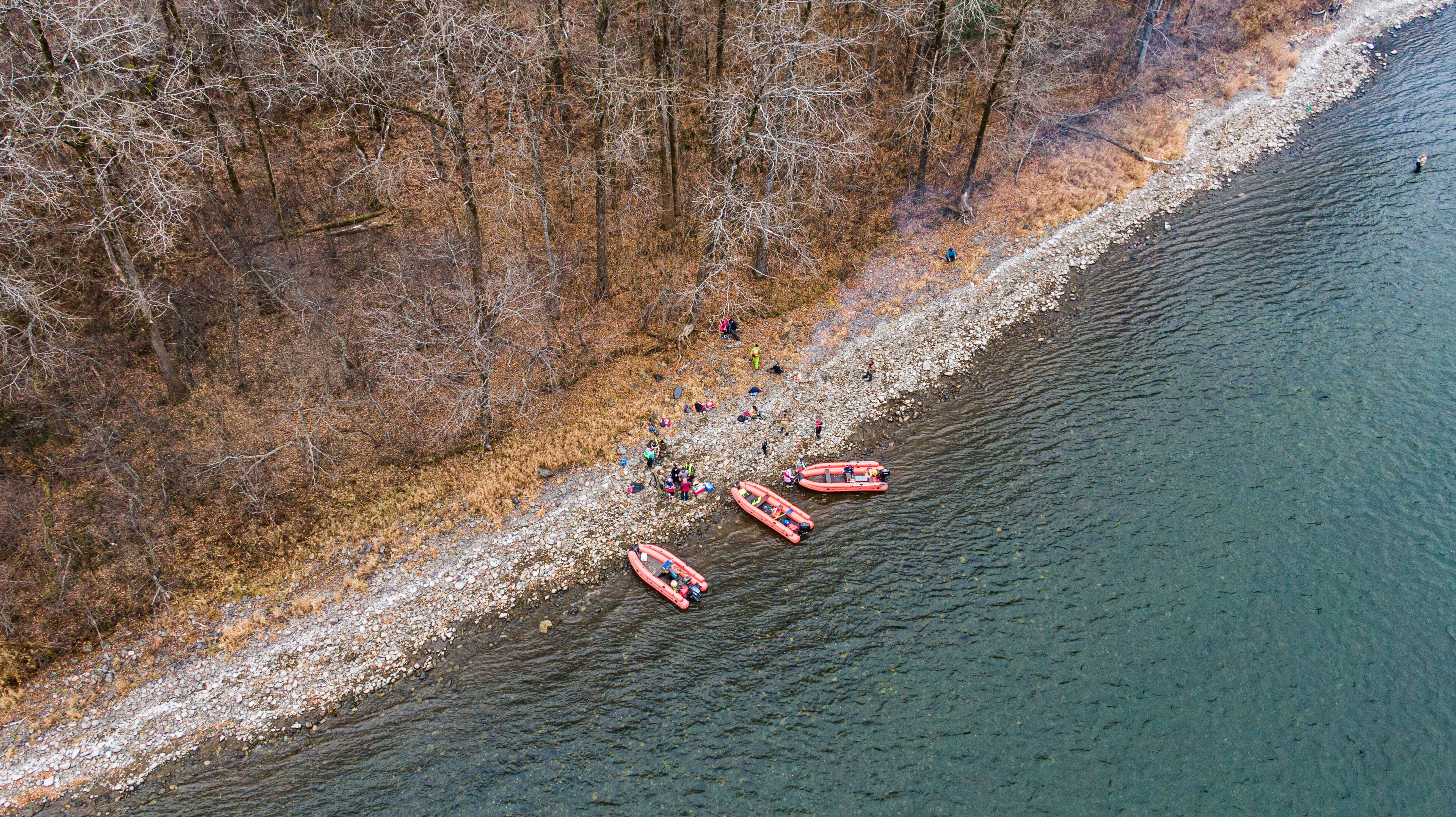 An aerial view of a riverbank with people and inflatable boats.