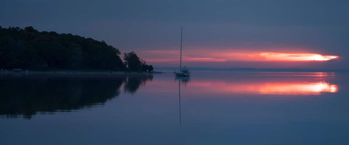 Sunrise over bay in northern Michigan with sailboat and foggy shore