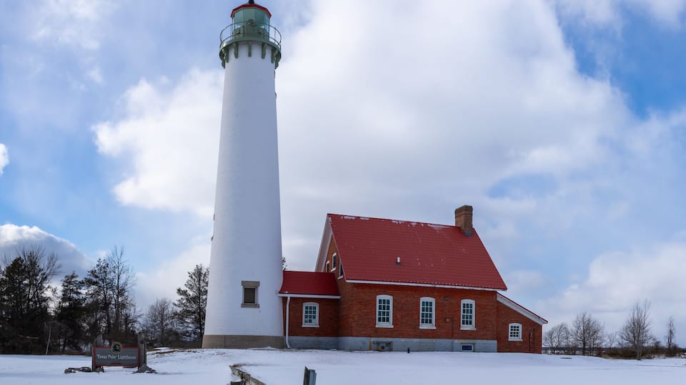 A lighthouse, a brick building, and a small white structure in a snowy landscape.