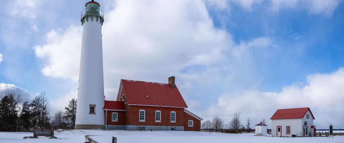 A lighthouse, a brick building, and a small white structure in a snowy landscape.