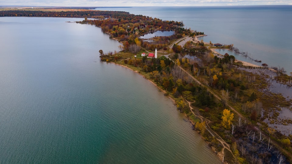 An aerial view of a coastal landscape with a lighthouse, a winding road, and a dense forest.