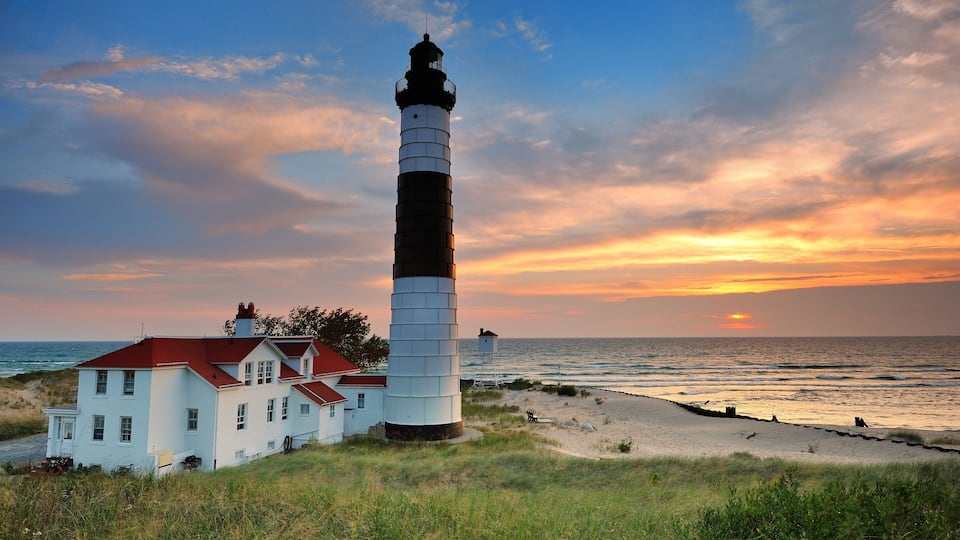 A lighthouse with a red roof, a white building, and a beach with waves.