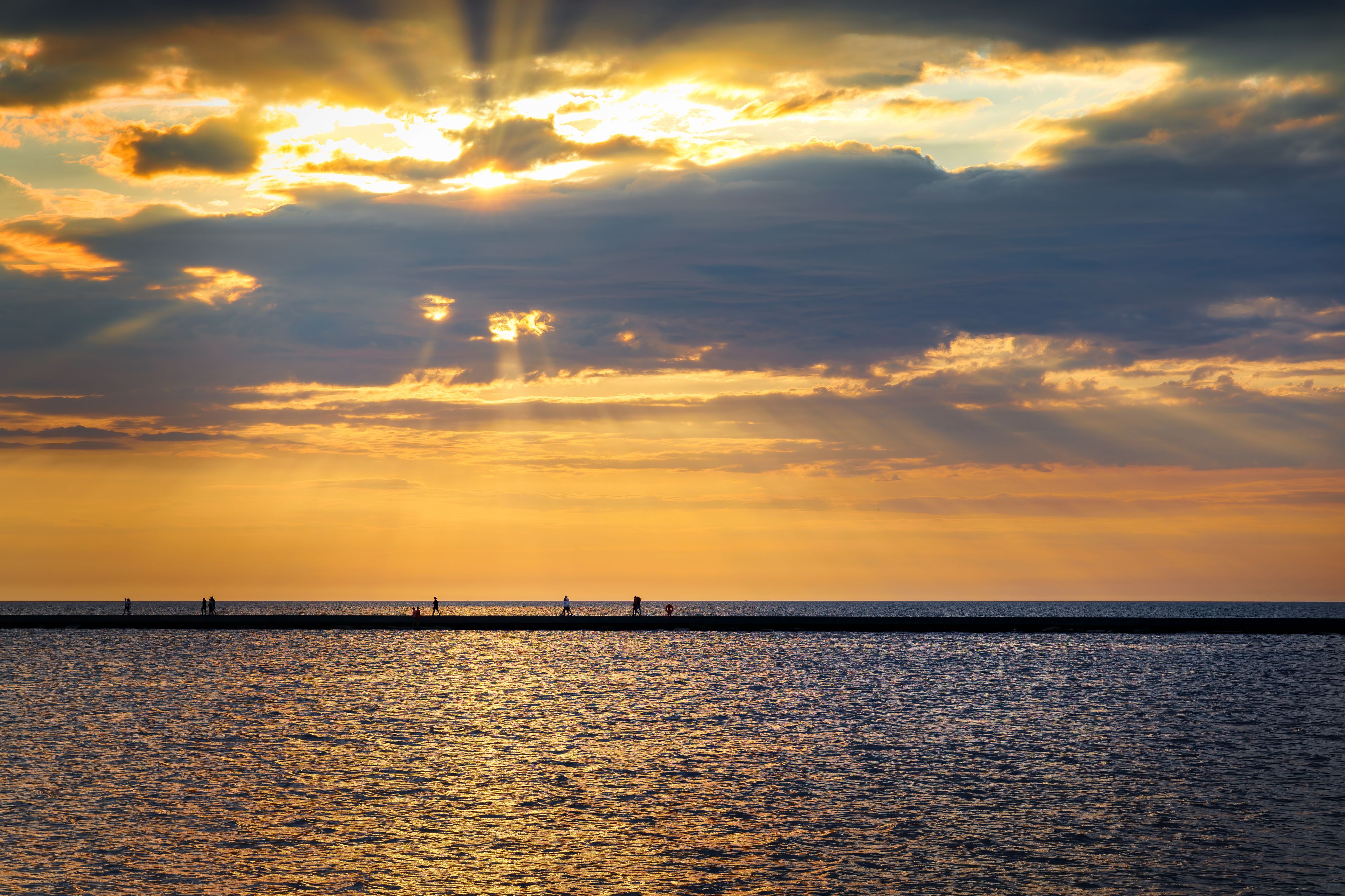 A sunset over a calm sea with a pier extending into the water.