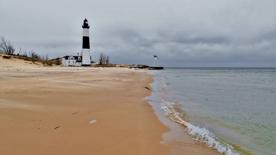 A lighthouse on a sandy beach with the ocean in the background.