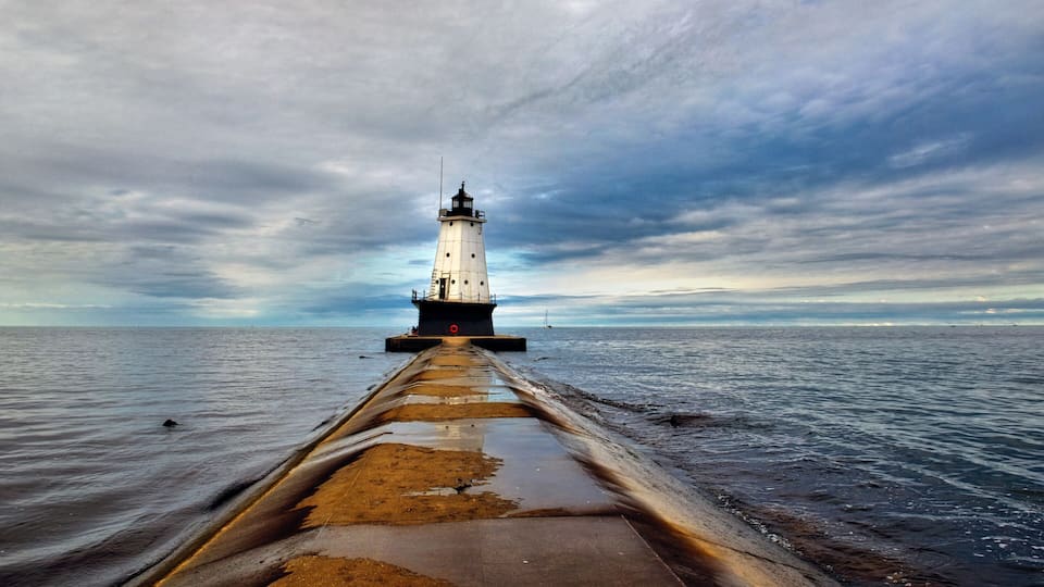 A lighthouse on a pier extending into the sea under a cloudy sky.