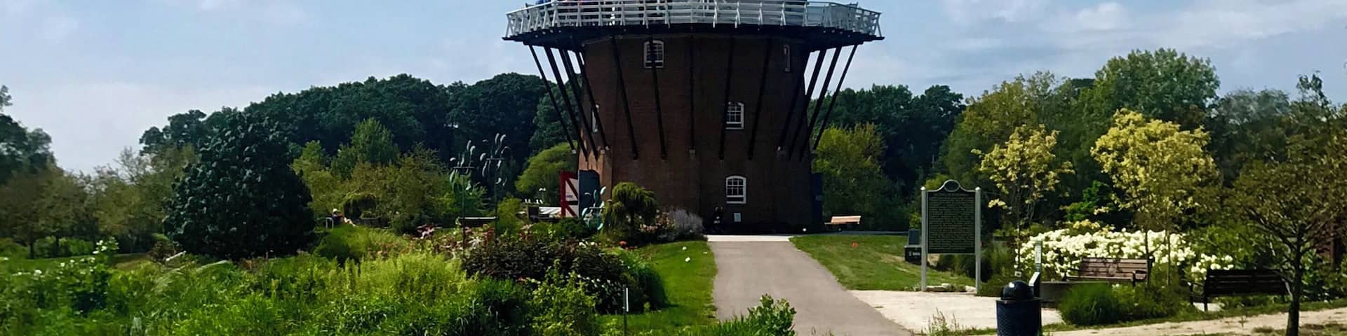 A windmill with a clear reflection in a pond surrounded by greenery.